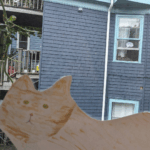 A paper cat in a window. In the background, a neighbouring cat has a speech bubble that says meow.